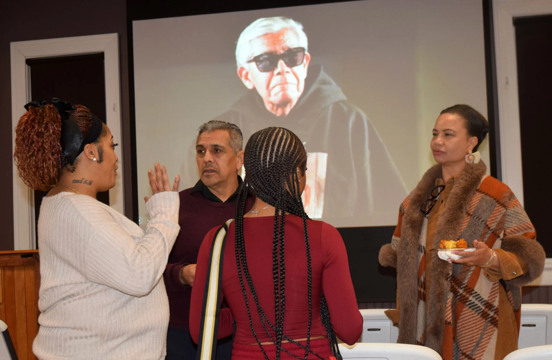 Tomecka Morton, left, Victor Tihopu, My-Lee Lambert and Lynn Tihopu visit after a Jan 20 reception to welcome a photography exhibit by Cecil Williams, who is shown in a recent picture in the backgroun. [photo courtesy of The Aiken Standard],
